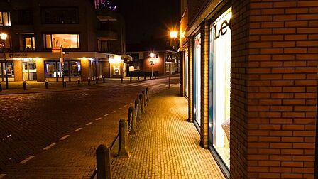 Schoutenstraat in Barneveld om middernacht. Het is een winkelstraat. Veel etages zijn verlicht. Op straat lijkt het daardoor donker