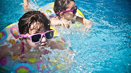Twee zwemmende kinderen met een zonnebril op.